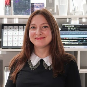 Alicja, Managing Director at Holts Gems in Hatton Garden, standing in the jewellery showroom with gemstone displays and awards behind her.
