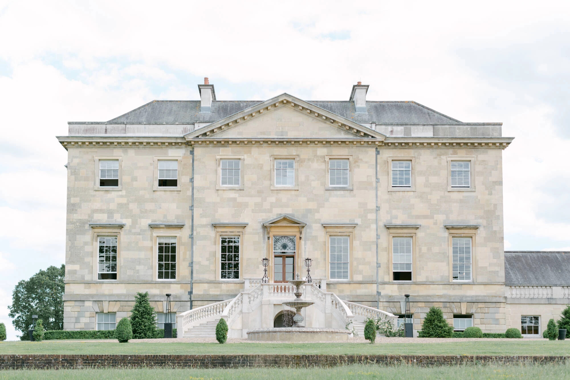 Front exterior of Botleys Mansion, a large stone country house wedding venue with central steps and fountain, set within landscaped gardens.