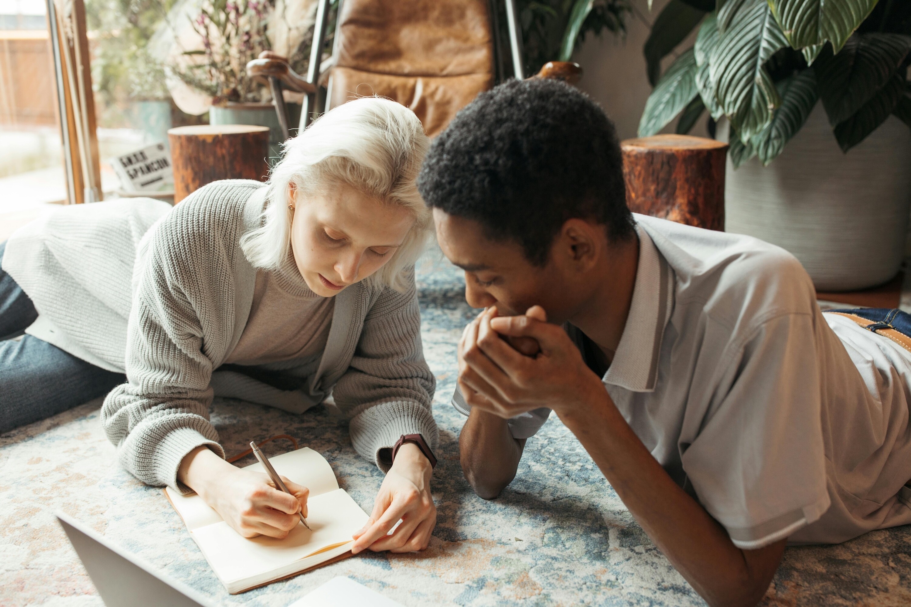 Couple sitting together at home writing notes and discussing plans while using a notebook and laptop.