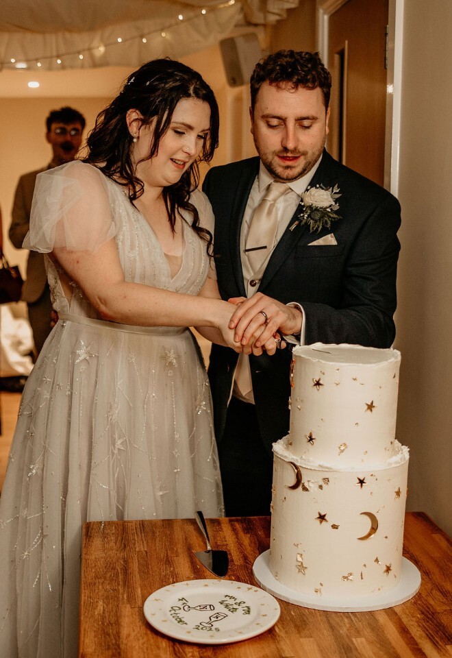 Bride and groom cutting a two-tier wedding cake with guests watching.