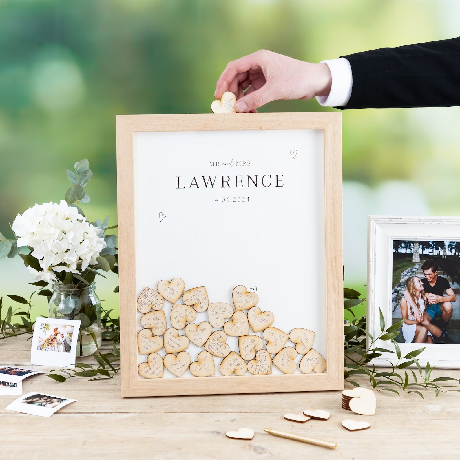 See-through box framed with wooden hearts inserted inside with wedding guest signatures.