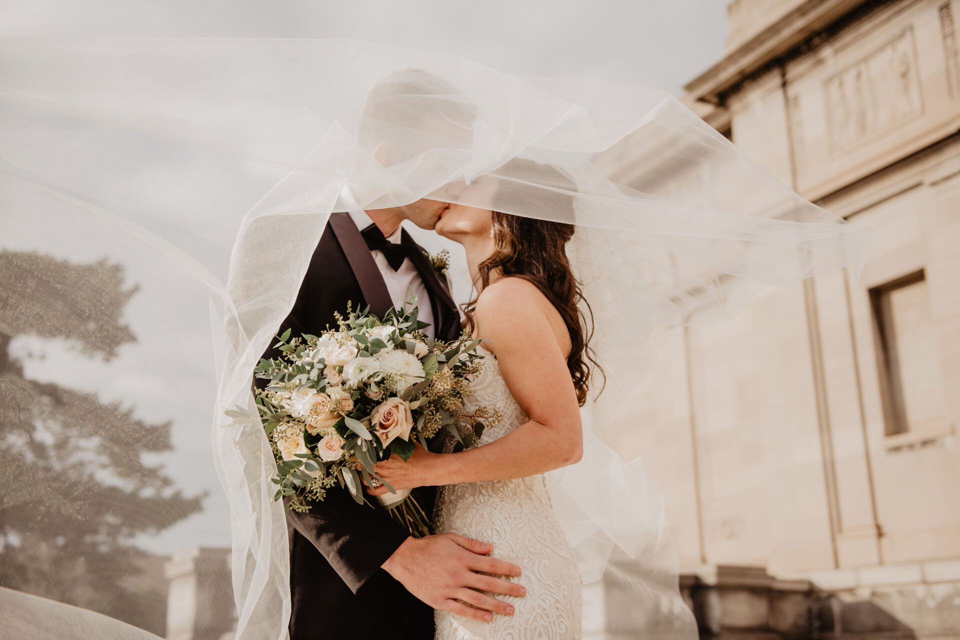 Newly married couple sharing a kiss beneath the brides veil outside a UK wedding venue