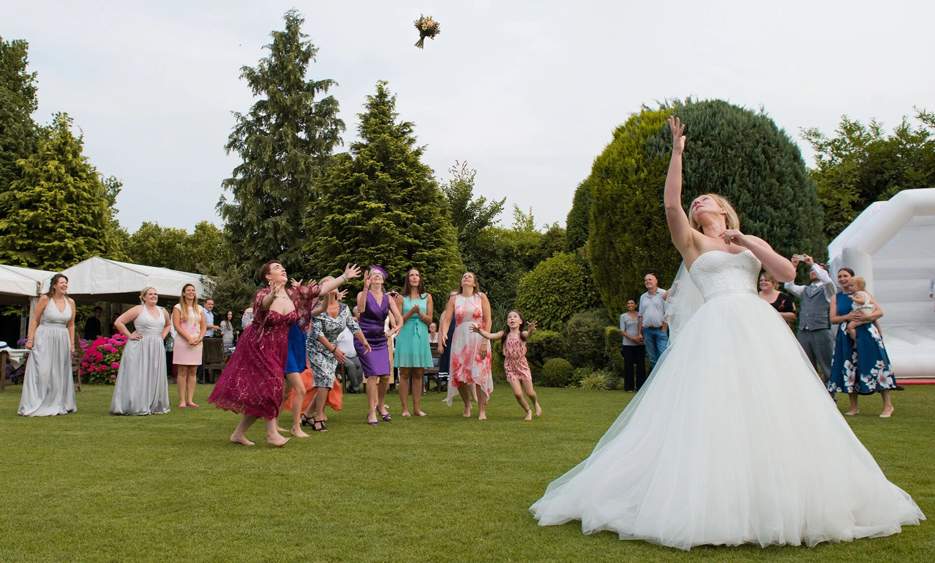 Bride throwing bouquet to bridesmaids and wedding guests in a garden. Taken by Paul Griffiths Photography, Oxfordshire