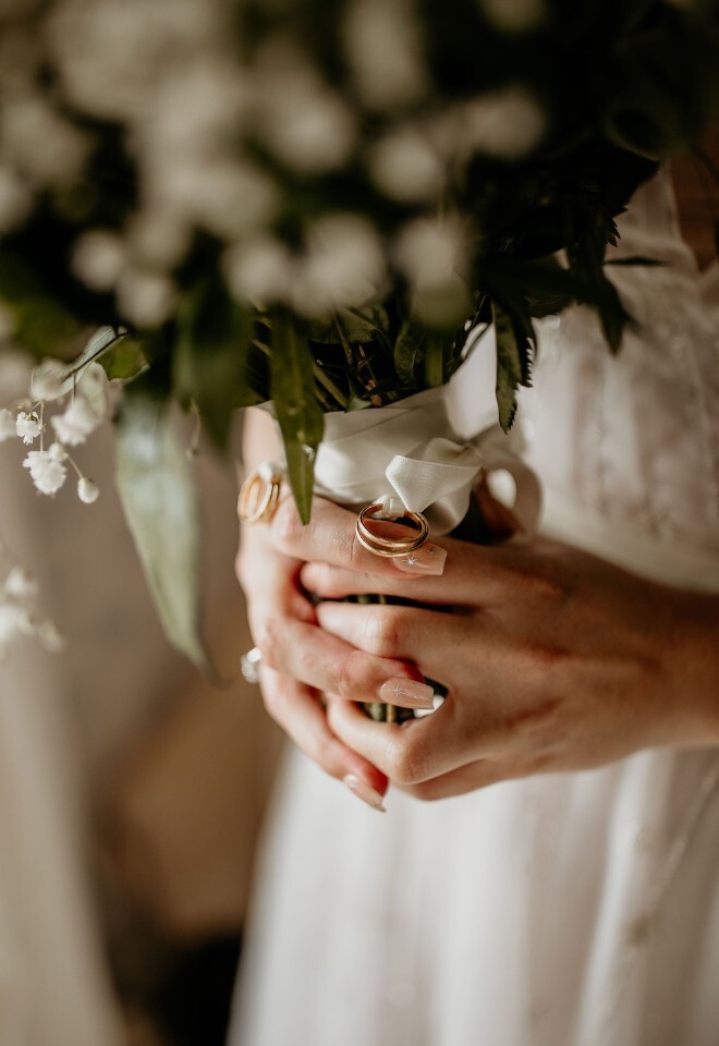 Bride holding a bouquet with wedding rings tied around the stems.