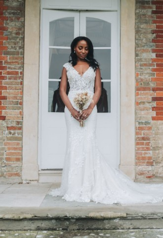 Bride wearing a lace, plunging neckline wedding dress, holding a bouquet, looking down