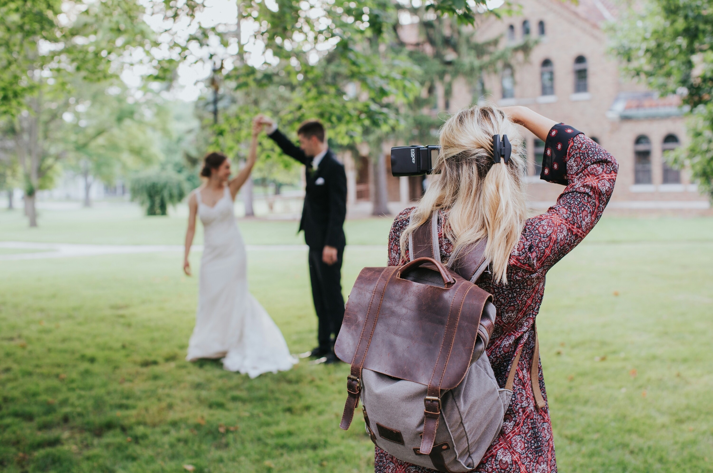 Wedding photographer capturing a couple dancing together outdoors, with the bride in a white dress and the groom in a black suit on a lawn in front of a historic building.