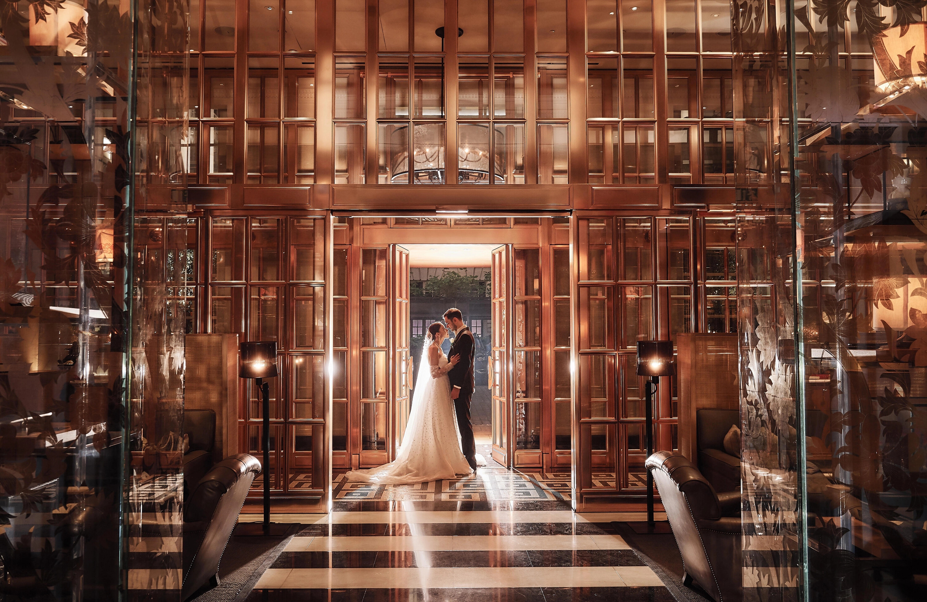 Photo of a wedding couple in a hotel lobby with glass walls and black-and-white tiled flooring. Taken by Stuart Wood Photography, Derbyshire.
