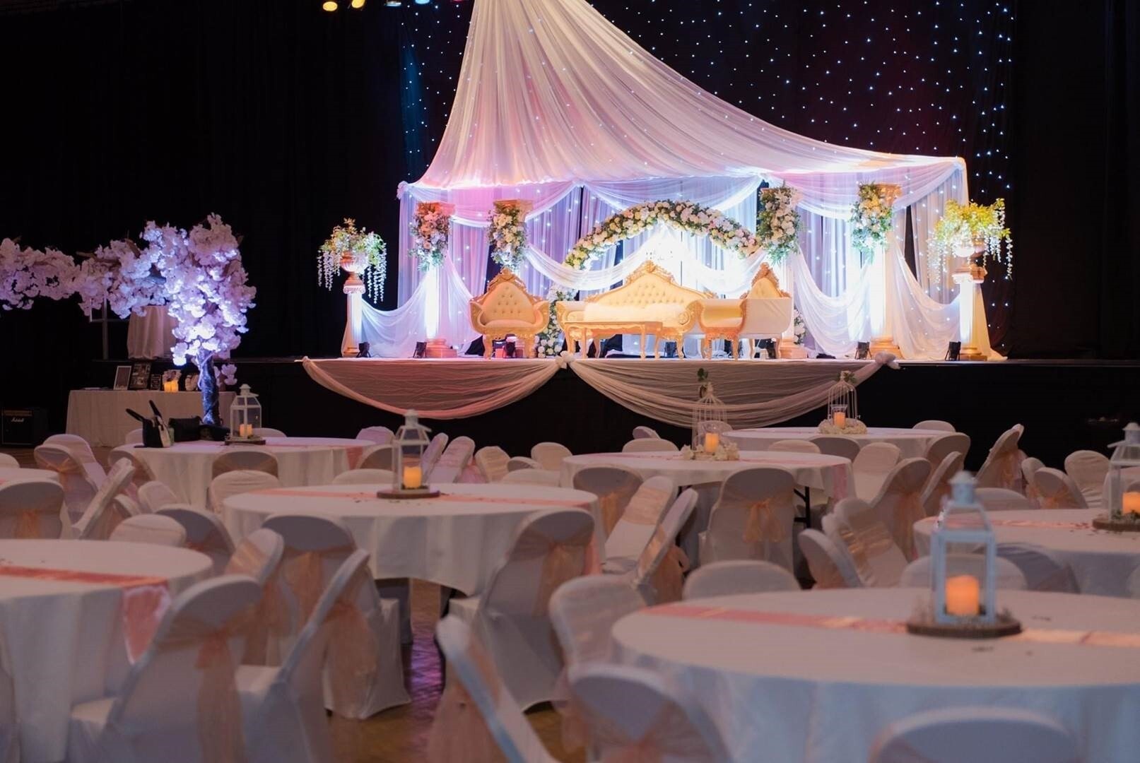 Charter Hall wedding venue in Essex set up for a large multicultural wedding reception with draped ceremonial stage, floral décor and banquet seating