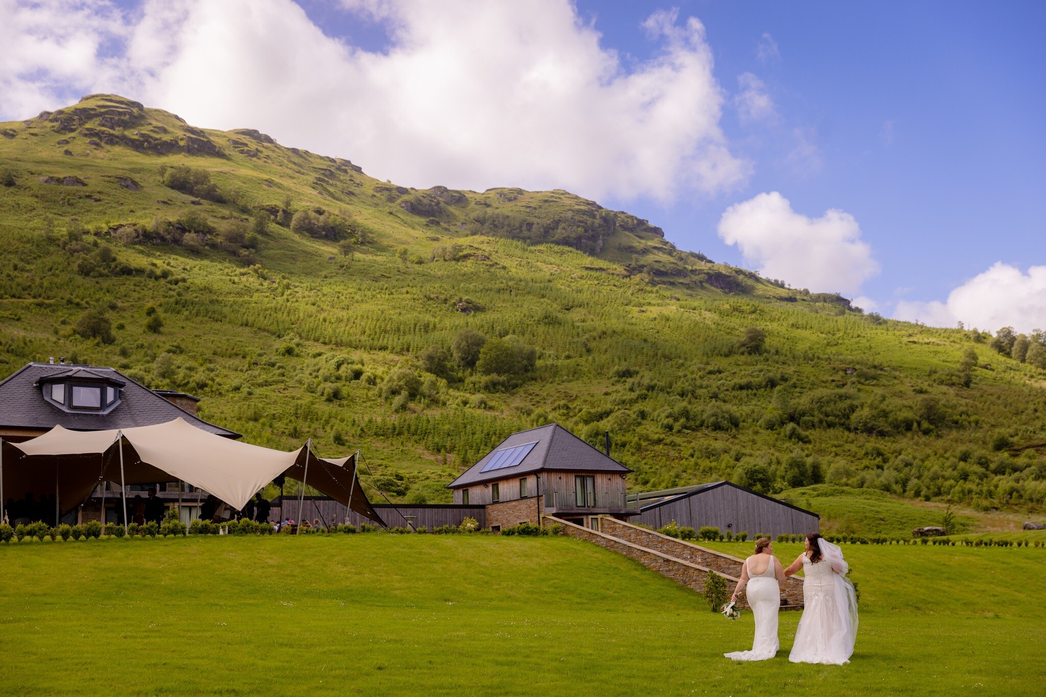 Bride and bride walk hand in hand towards Carrick Castle Estate