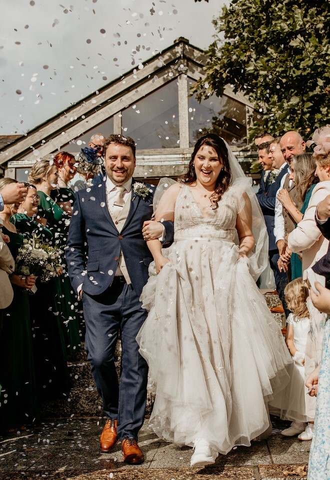 Newlyweds walking through confetti as guests celebrate outside the venue