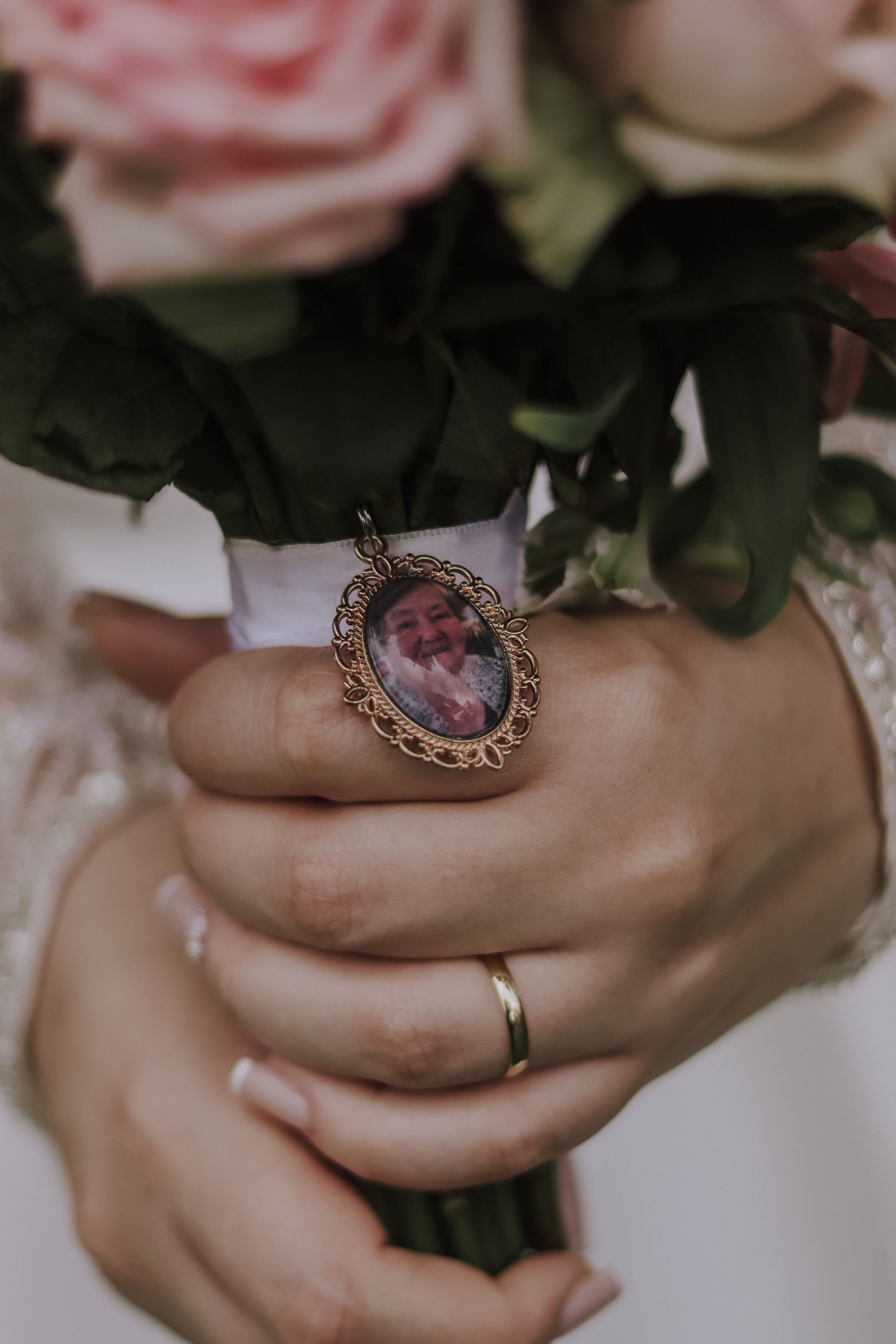 Bride holding a wedding bouquet with a photo charm in memory of a loved one who has passed away.