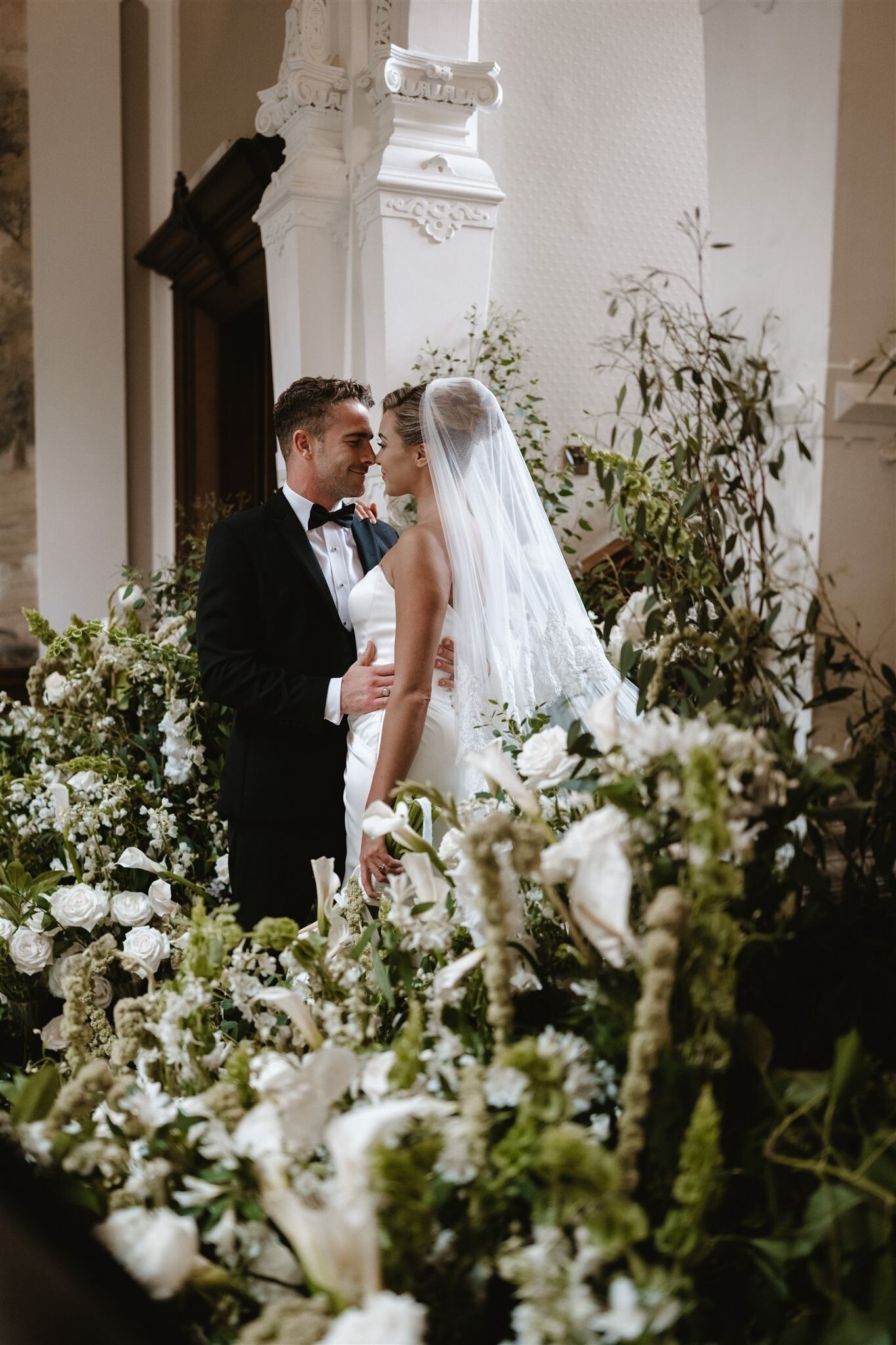 Bride and groom stand between white and green wedding floral arrangement