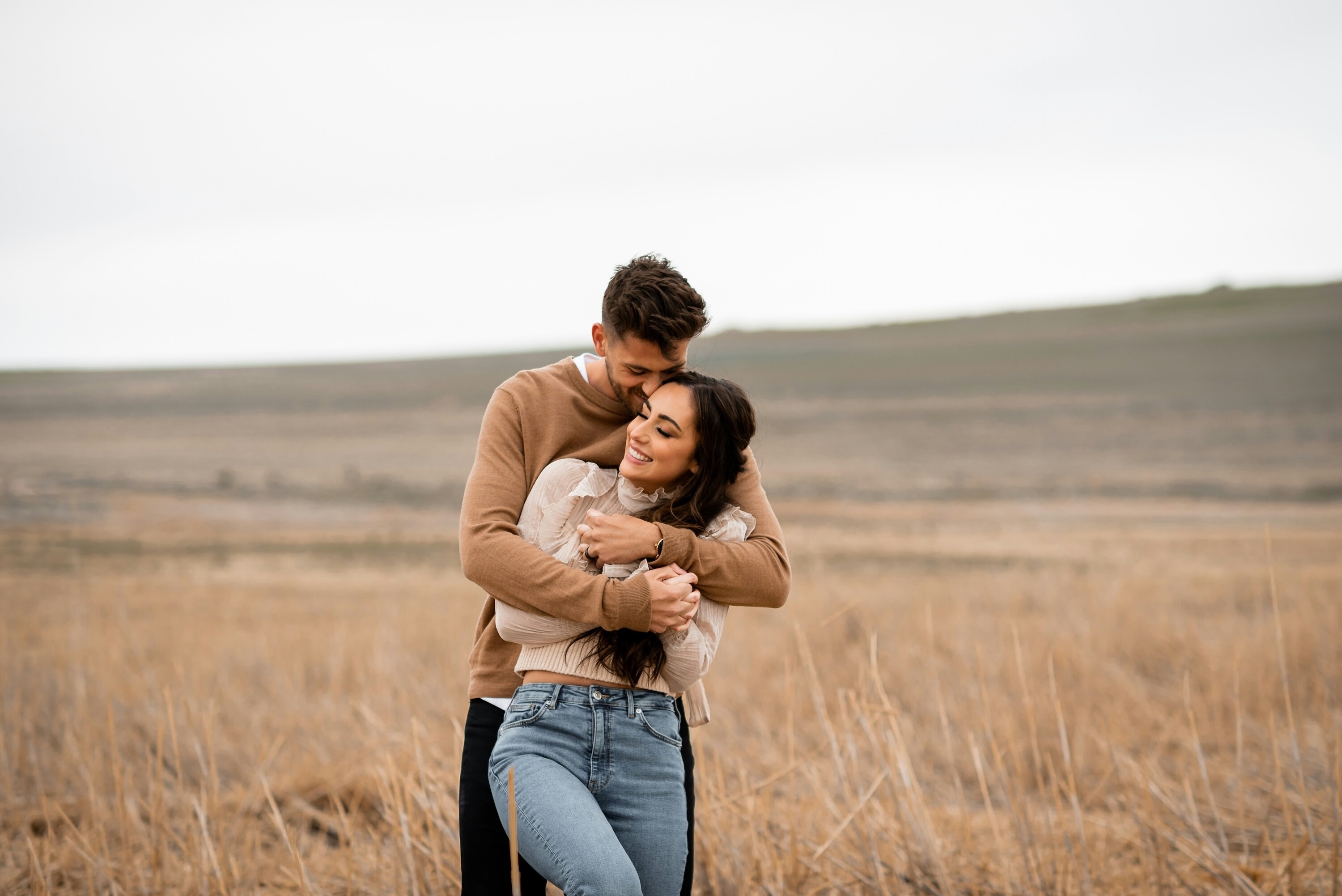 Engaged couple with arms wrapped around each other in a field during their outdoor engagement photoshoot.