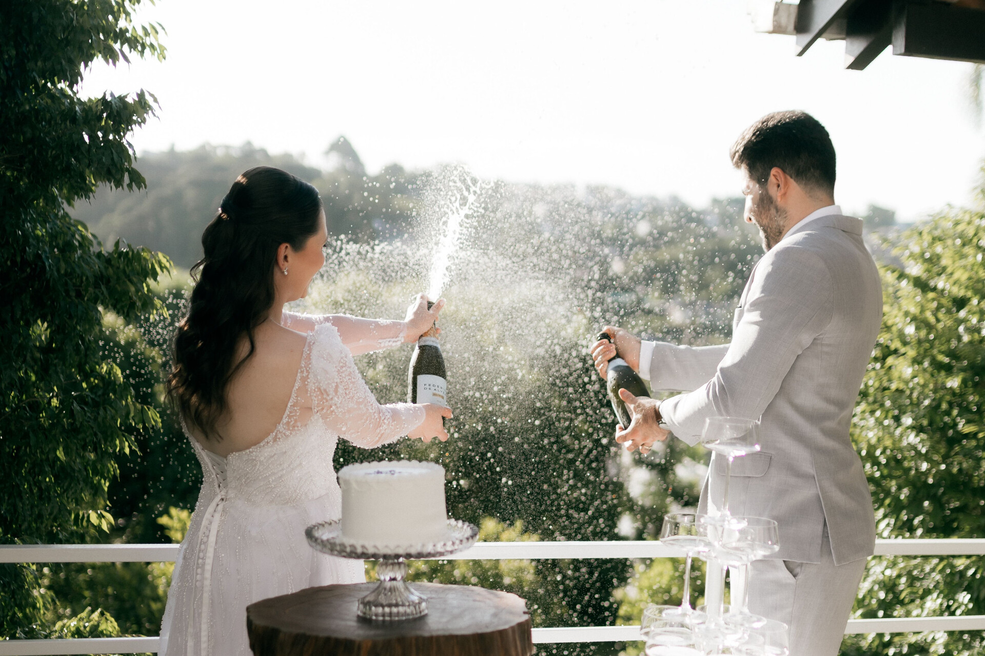 Newlyweds celebrating with a champagne spray during an outdoor wedding reception.