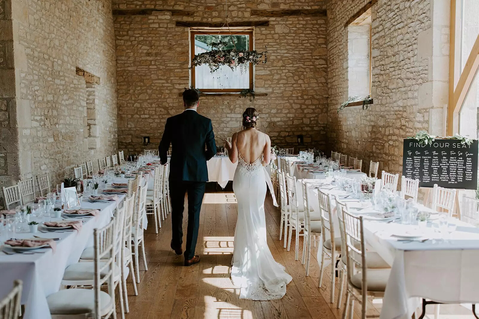 Interior set for a wedding breakfast, bride and groom walk through centre of the room before guests are seated.