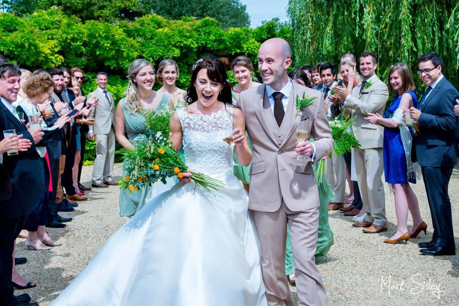 Wedding photo of bride and groom walking through a walkway of guests with champagne in hand. Taken by Mark Sisley Photography, Buckinghamshire