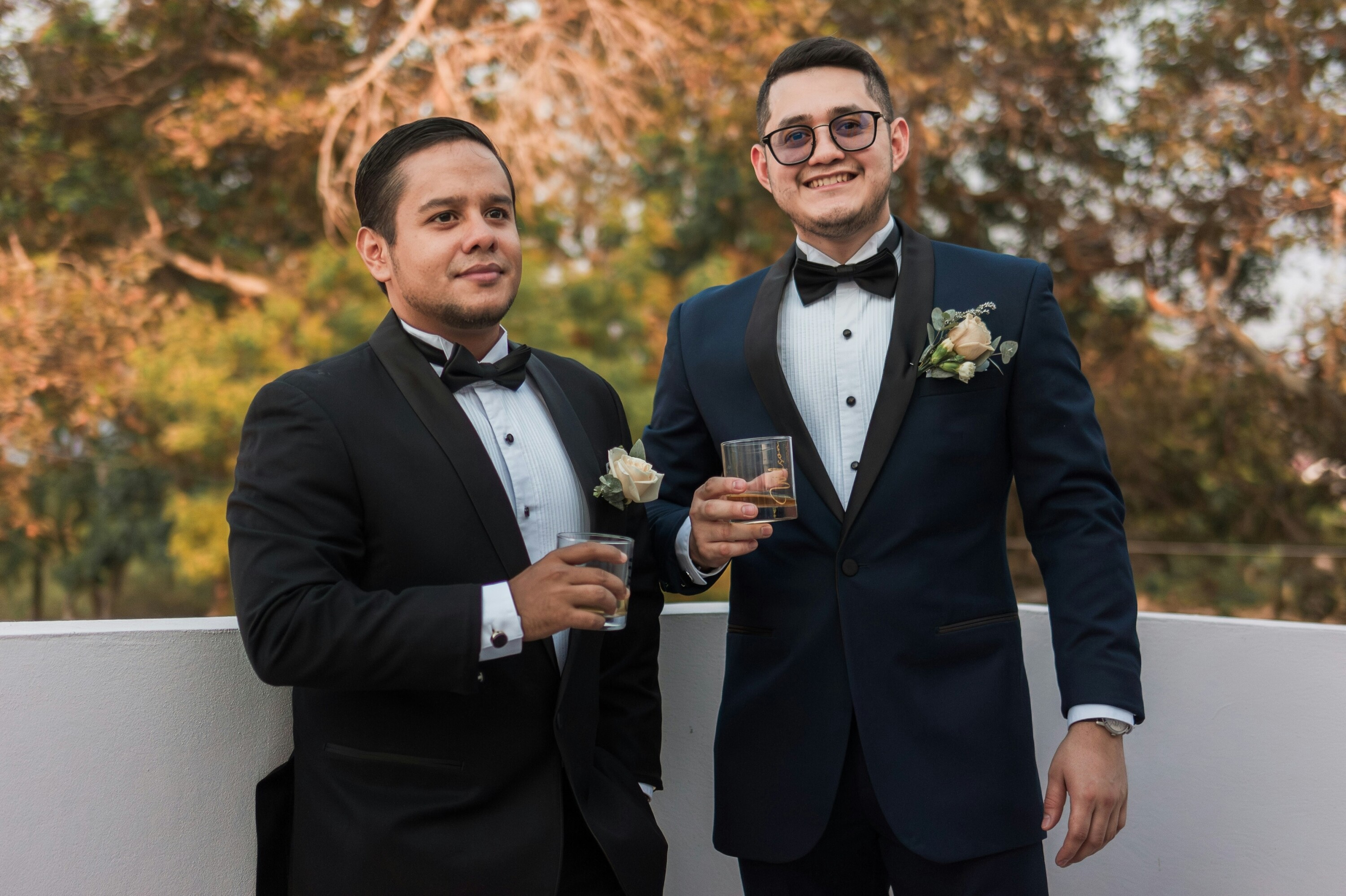 Groom and usher holding glasses and smiling at camera