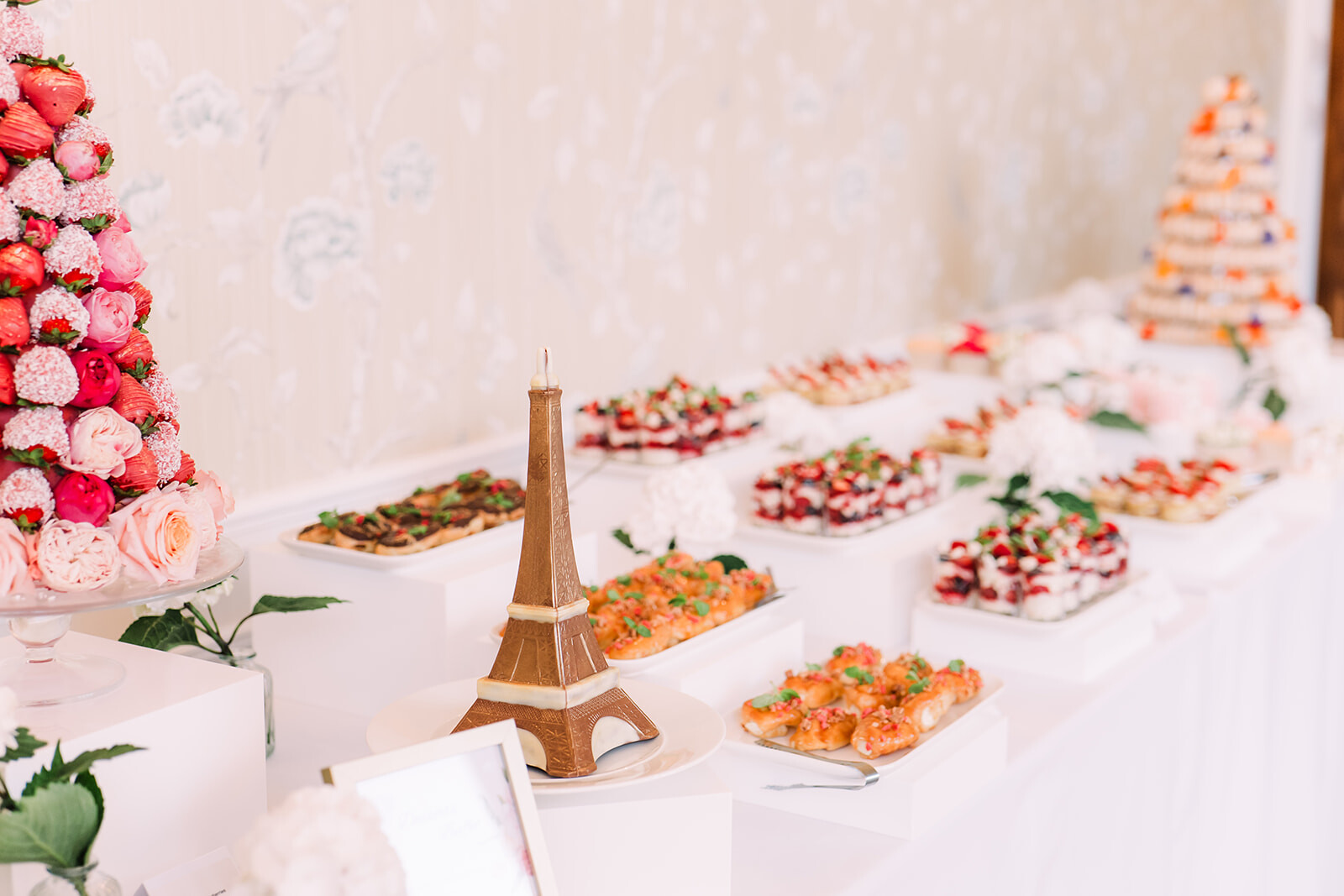 Paris-inspired wedding dessert table with Eiffel Tower cake, floral display and elegant French-themed pastries.