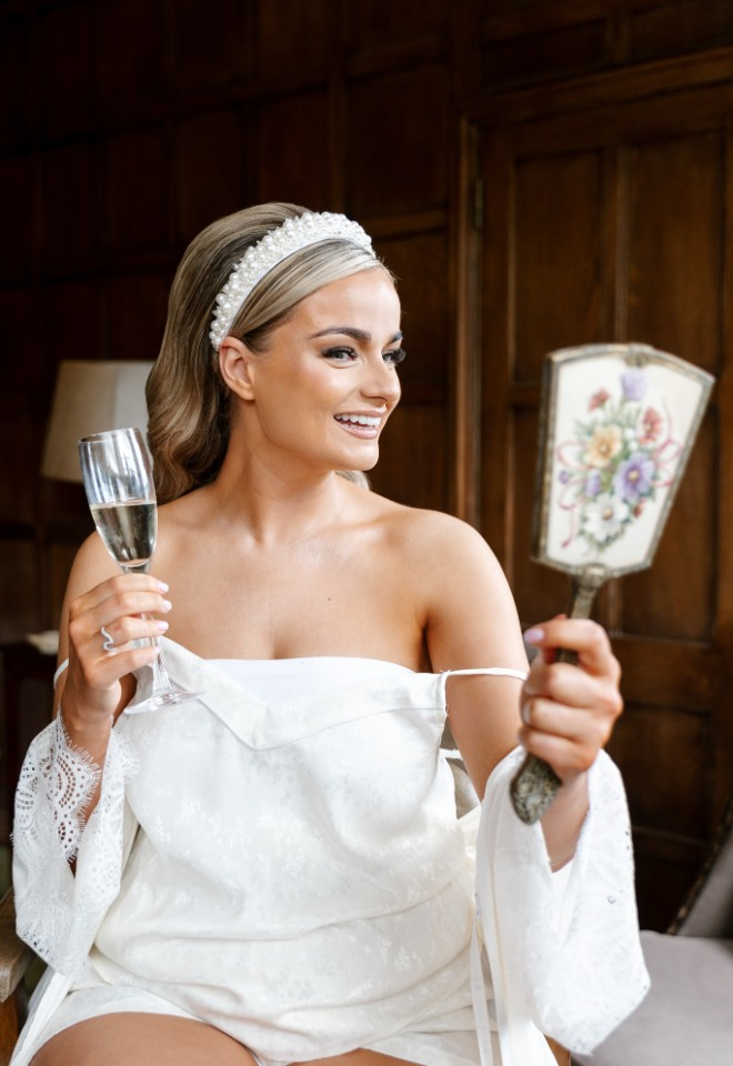 Bride admiring her hair and makeup in small handheld mirror on wedding morning