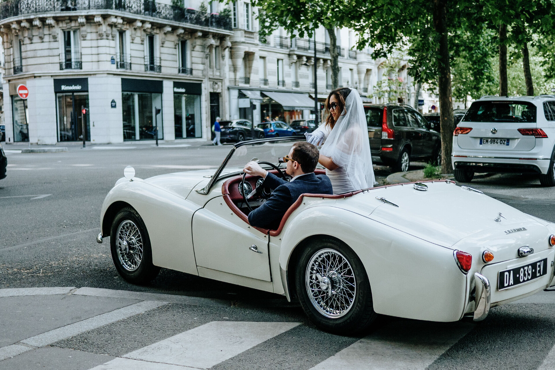 Bride and groom travelling in a classic white convertible as part of their luxury wedding celebration.