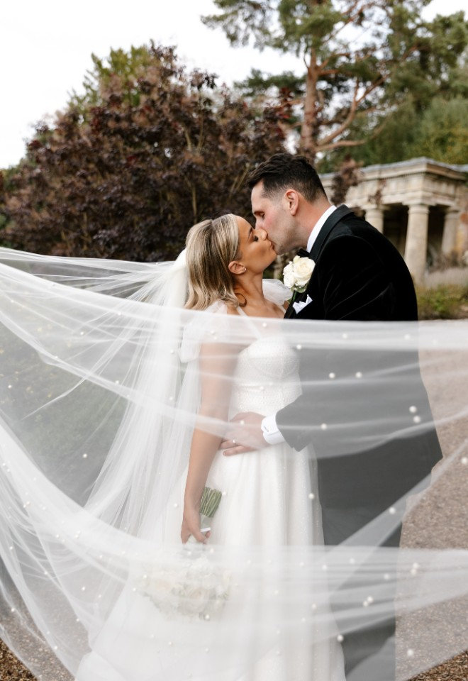 Bride and groom kiss with veil in front of them