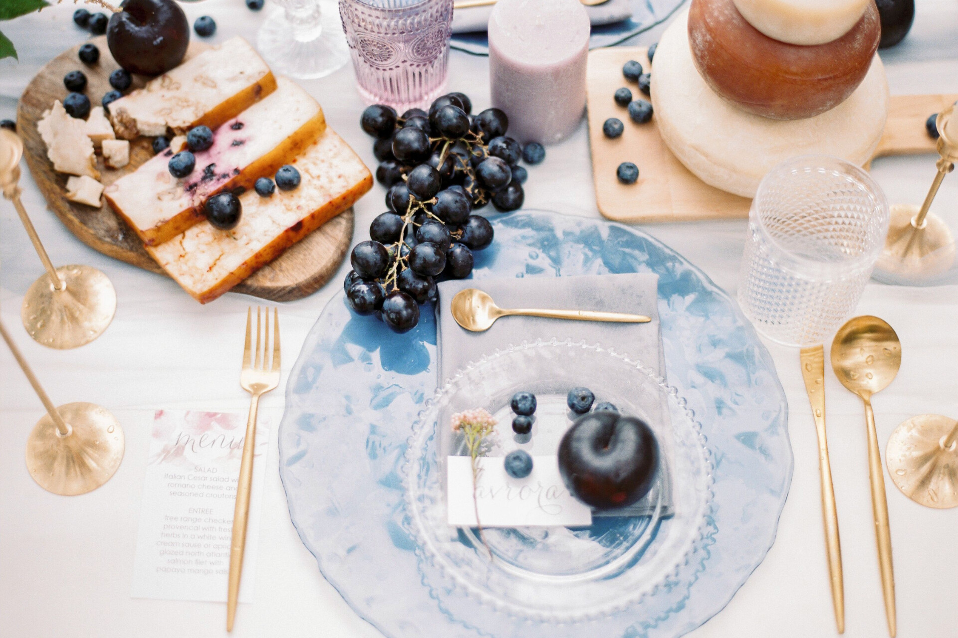 Elegant wedding tablescape featuring layered place settings, artisanal cheeses, fresh fruit and gold cutlery.
