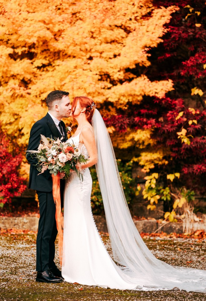 Bride and Groom kissing in front of the autumn leaves