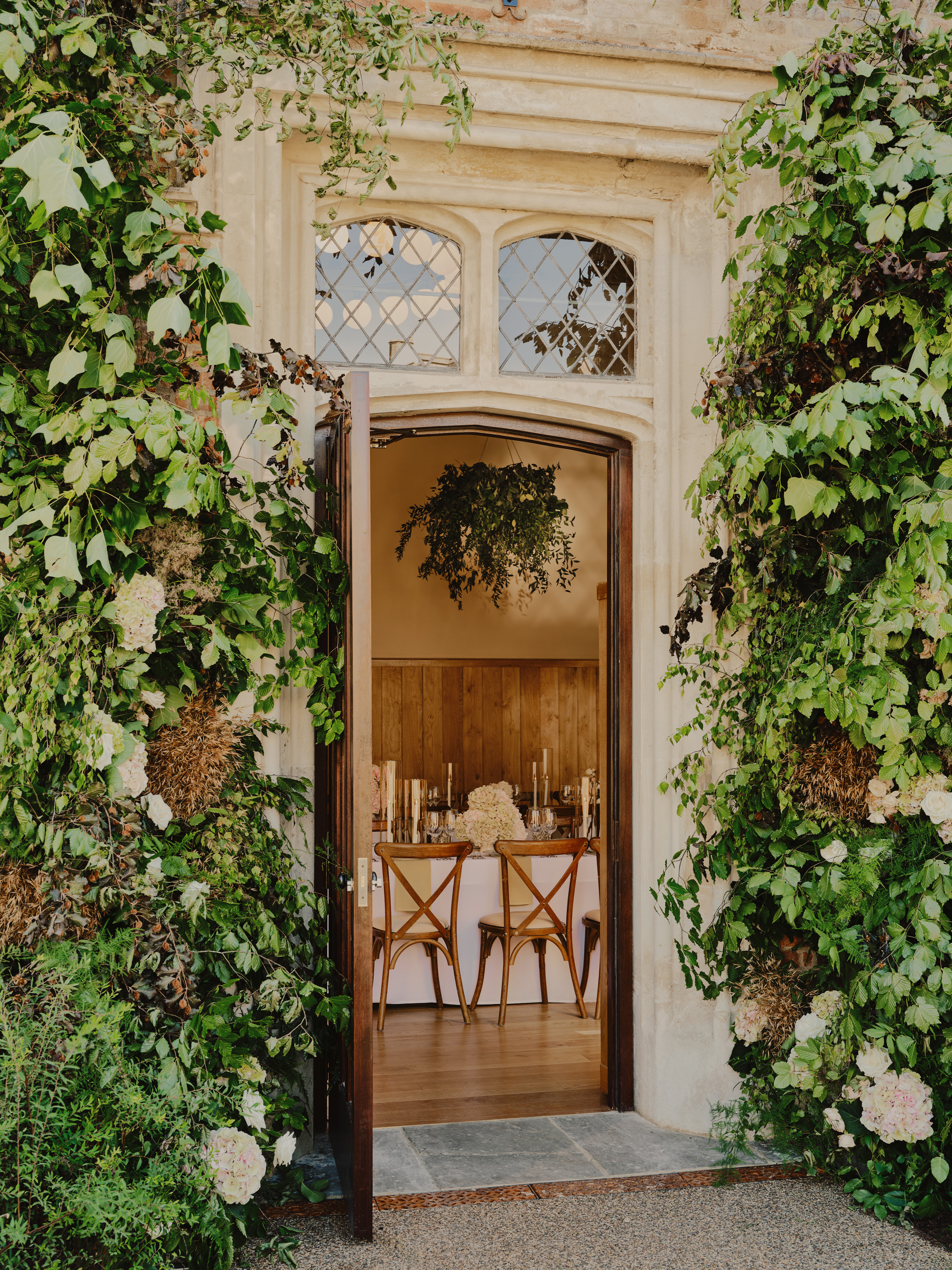 Foliage lined doorway with a oak wooden door leading into a wedding breakfast setup at Dukes Yard