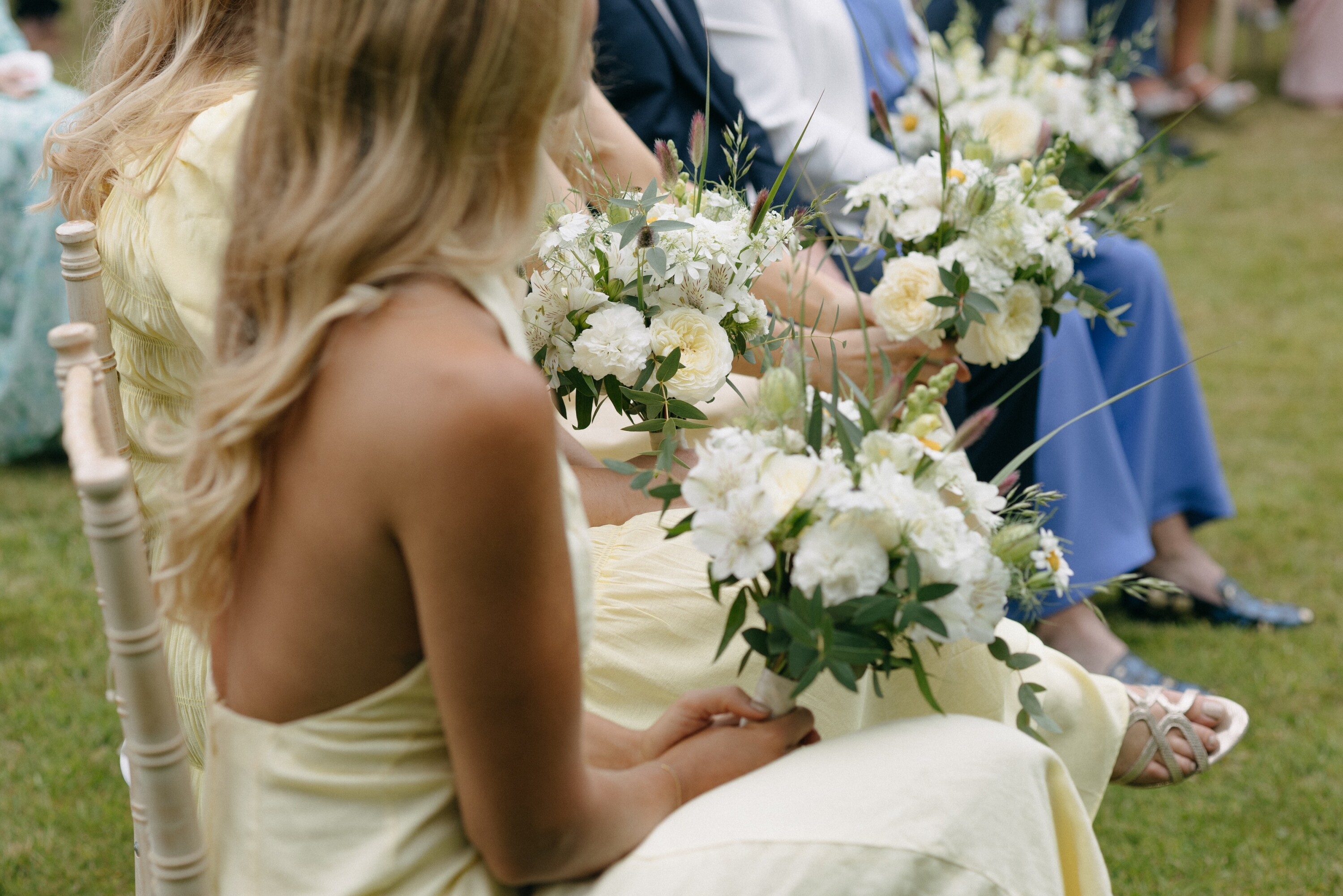 Bridesmaids holding butter yellow bouquets at the wedding ceremony