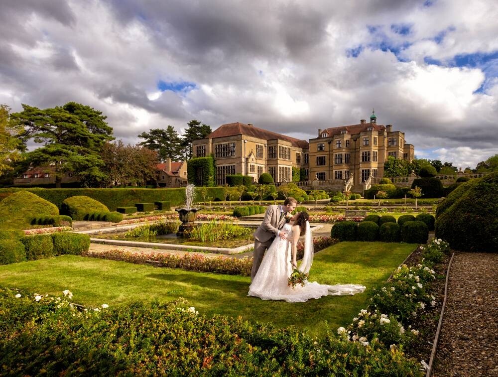 Couple in formal gardens at Fanhams Hall in Hertfordshire, with the country house and landscaped grounds in the background