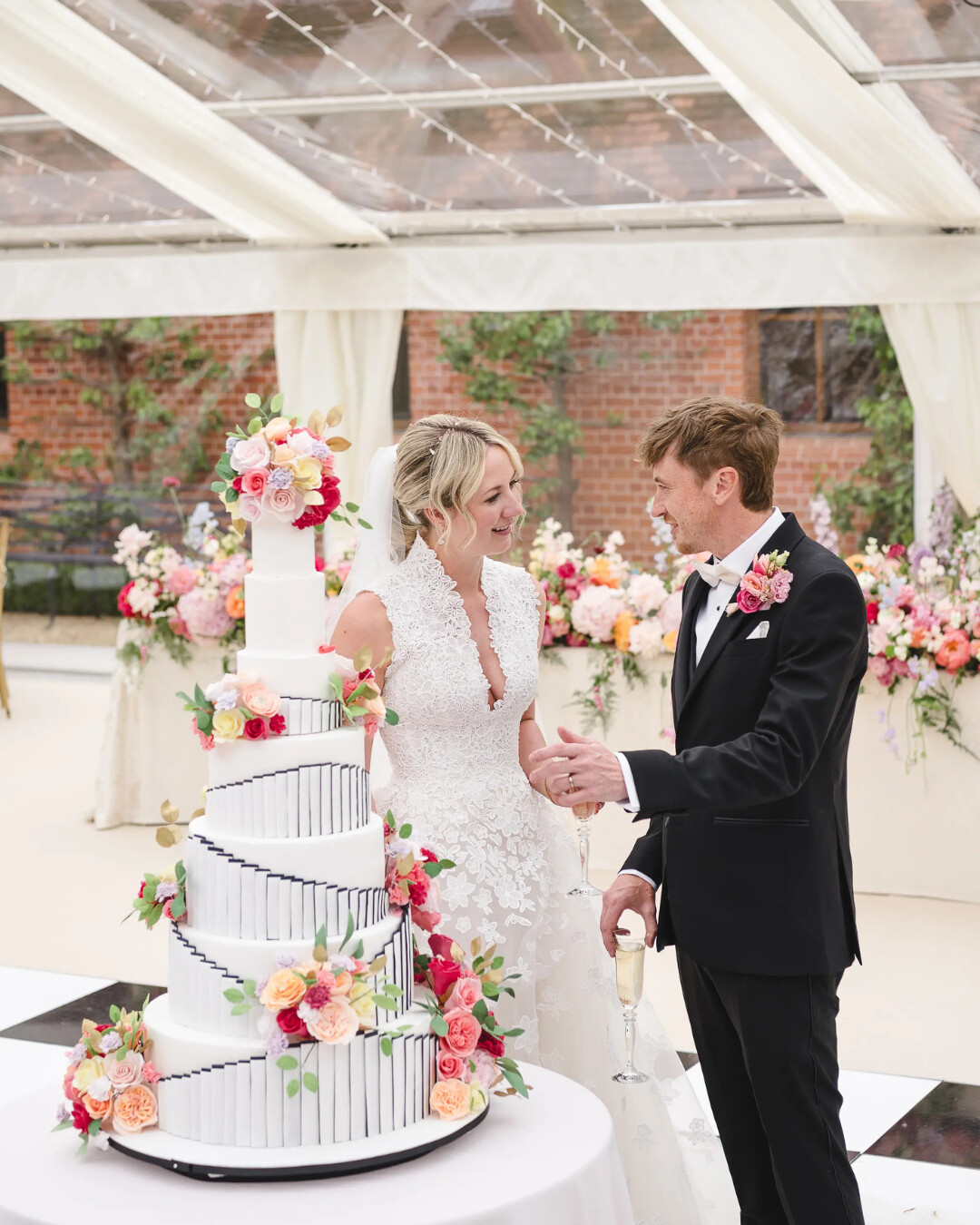 Bride and Groom cutting 7-tier wedding cake with bright florals, created by Nicola hall - owner of Hall of Cakes