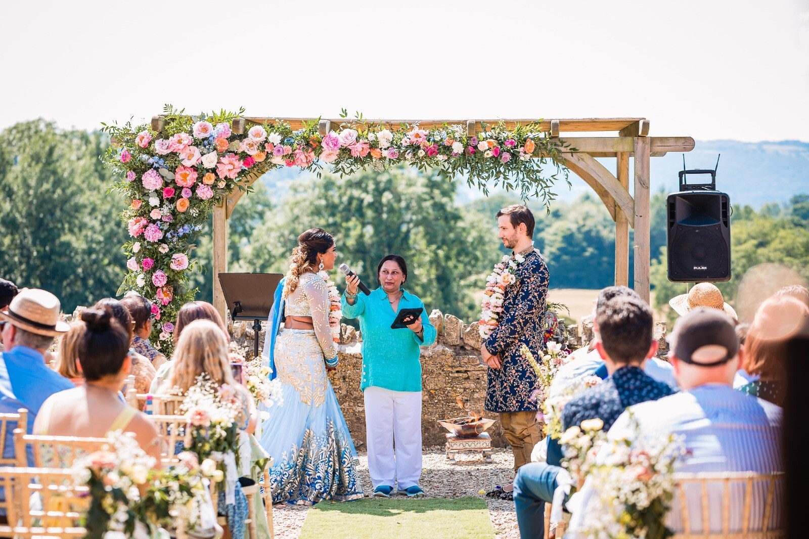 Sonal Dave, Independent celebrant leading a multicultural outdoor wedding ceremony, with the couple exchanging vows beneath a floral arch as guests look on.