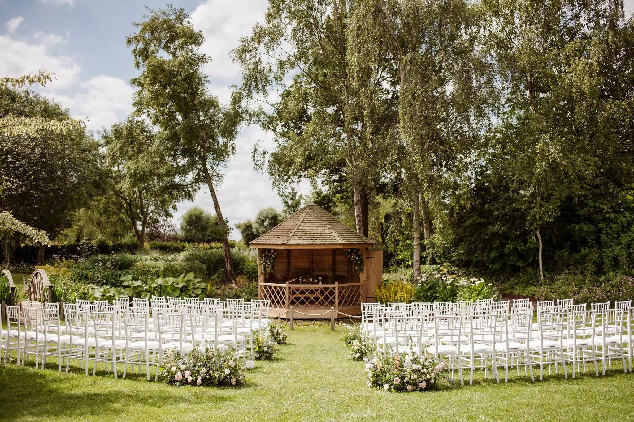 Outdoor wedding ceremony setup at South Farm with a wooden gazebo, white chairs and garden surroundings