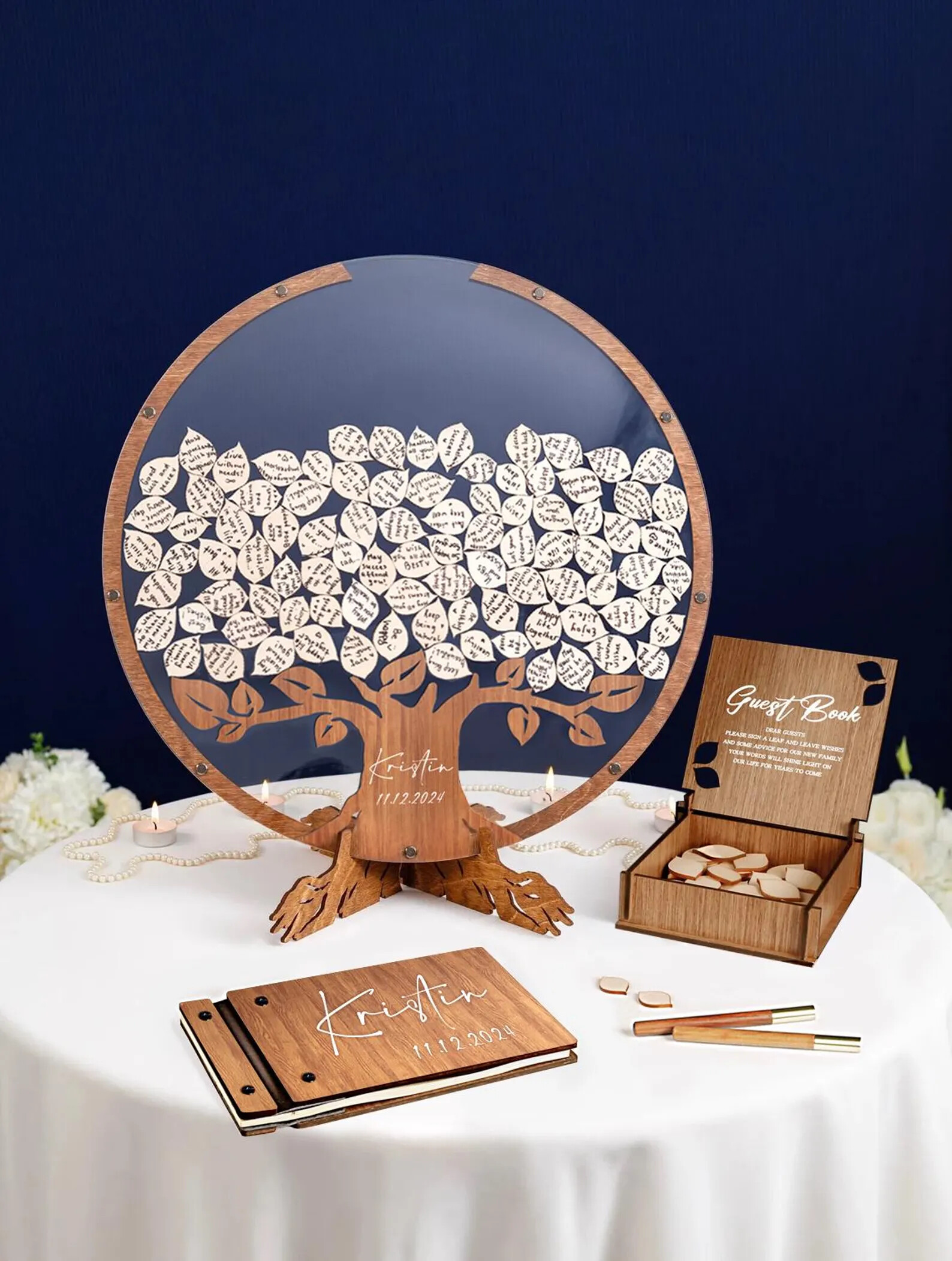 Wooden tree guest book alternative with a clear circular frame, where guests sign small leaf-shaped pieces and place them onto the tree, displayed alongside a matching sign and storage box.