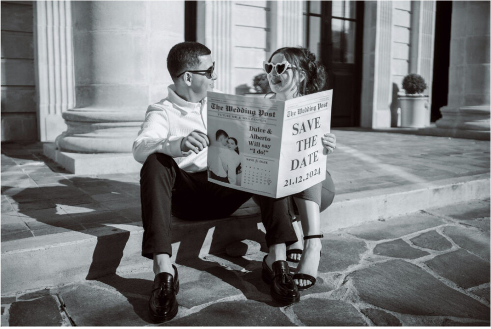 A couple reading a wedding newspaper that says "save the date"