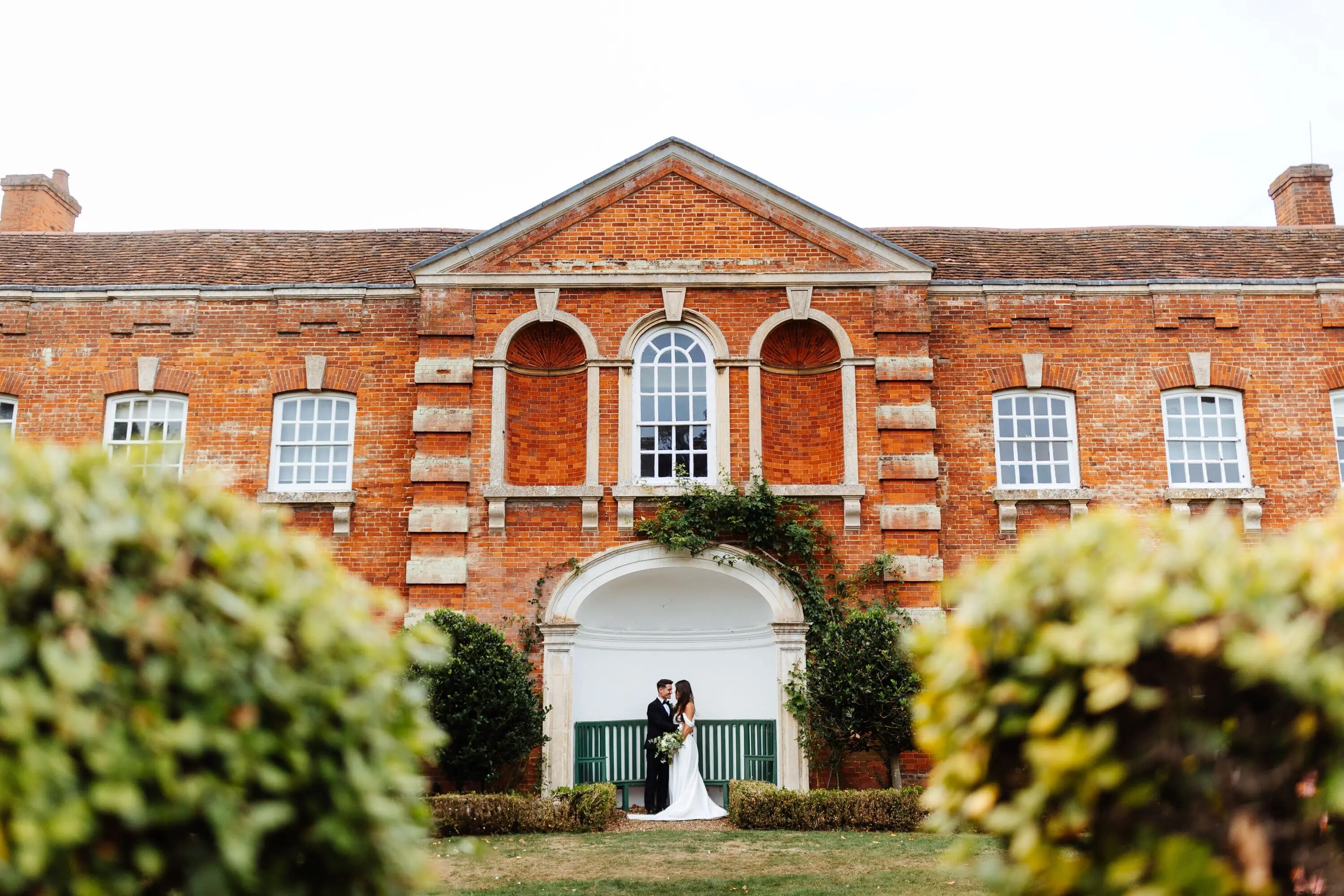 Bride and groom standing in the grounds in front of the exterior of Chicheley Hall