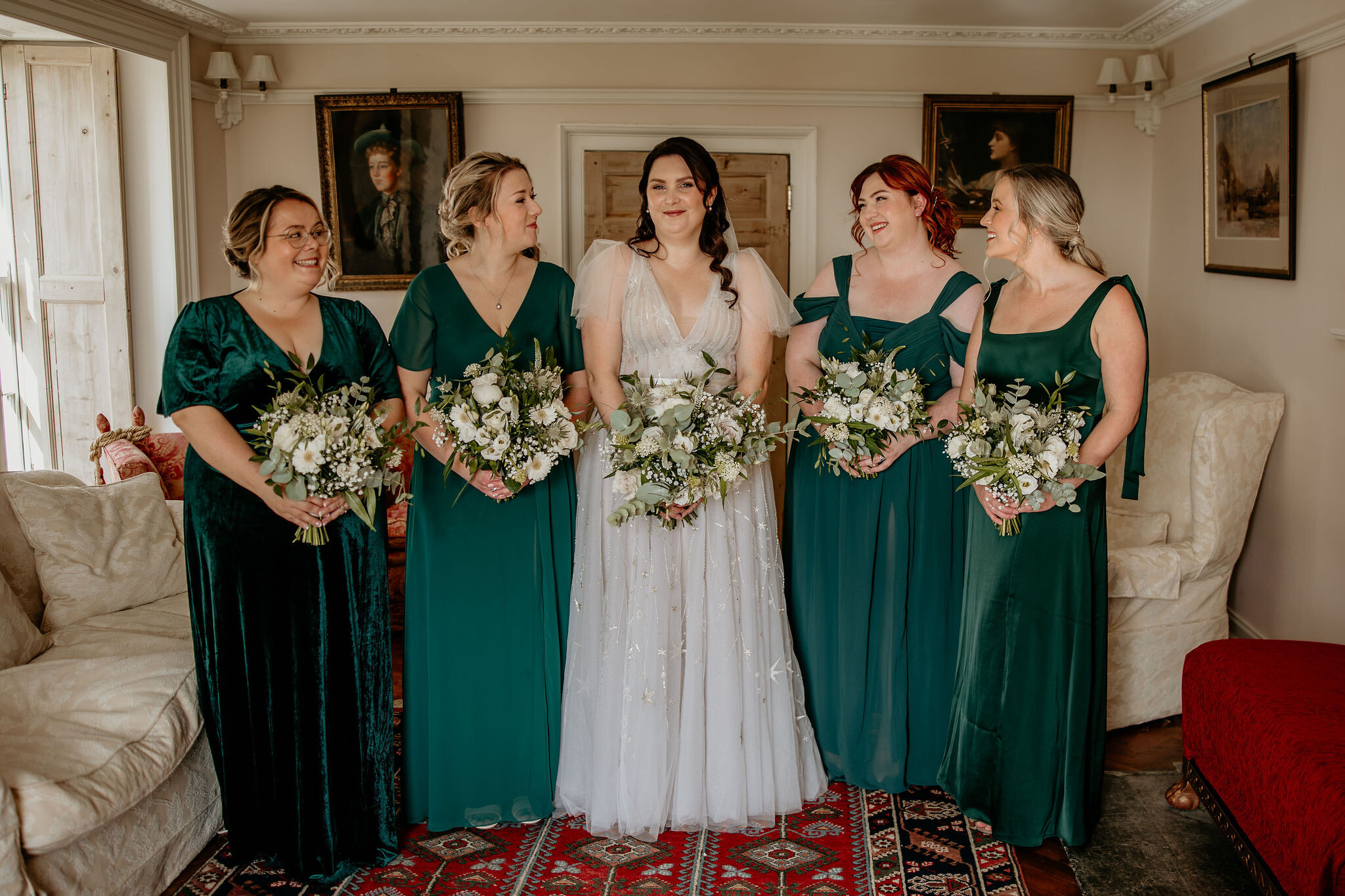 Bride in her wedding dress with her bridesmaids dressed in dark green mismatched dresses