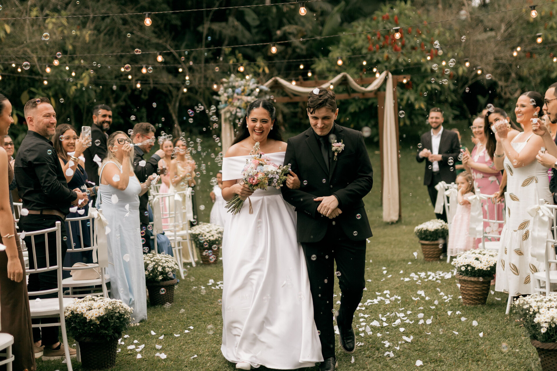Newly married couple walking down the aisle as guests celebrate during an outdoor garden wedding