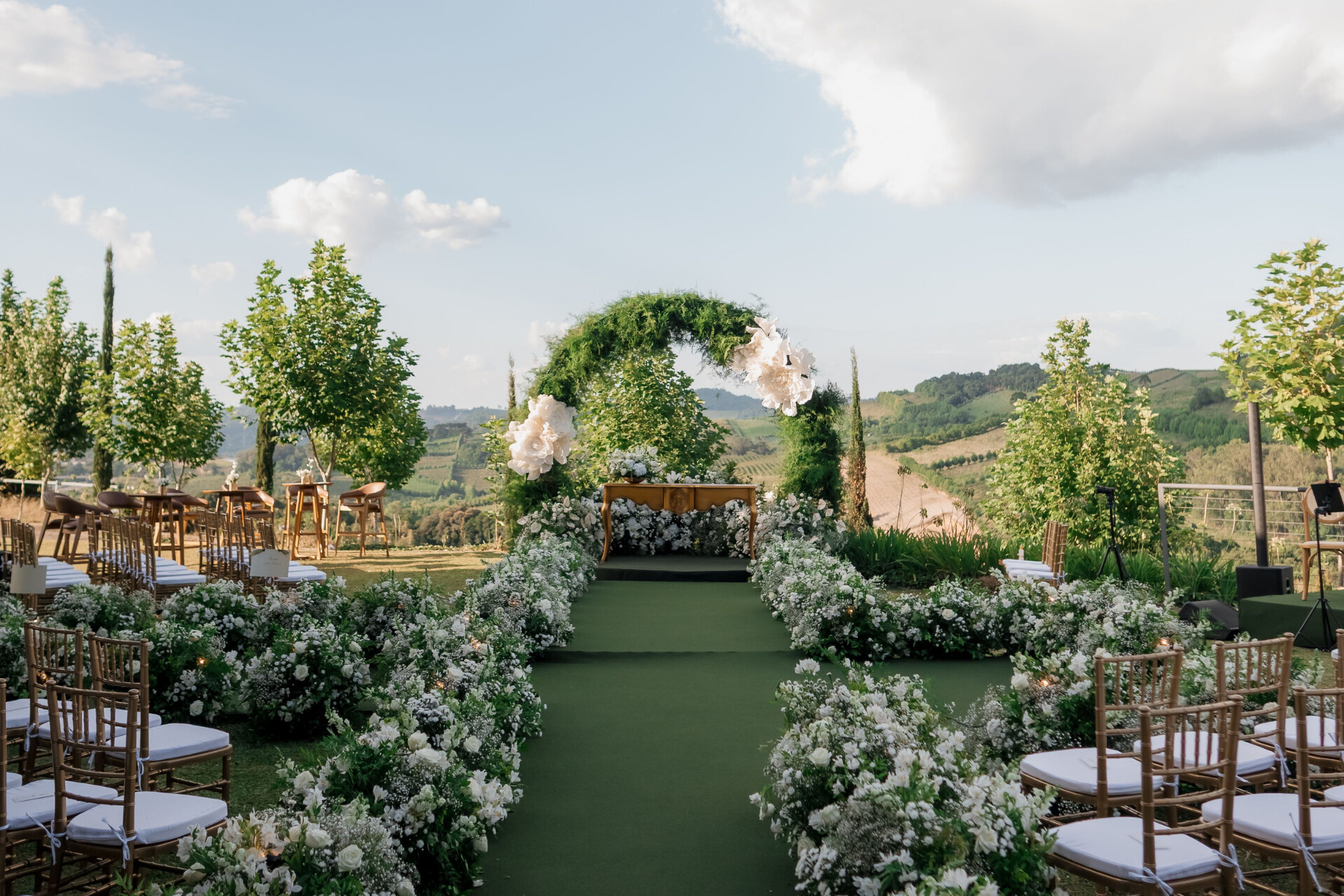 Luxury outdoor wedding ceremony featuring a flower-lined aisle and statement greenery arch overlooking the countryside.