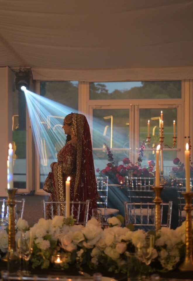 Bride standing under the spotlight between the decorated tables in the marquee