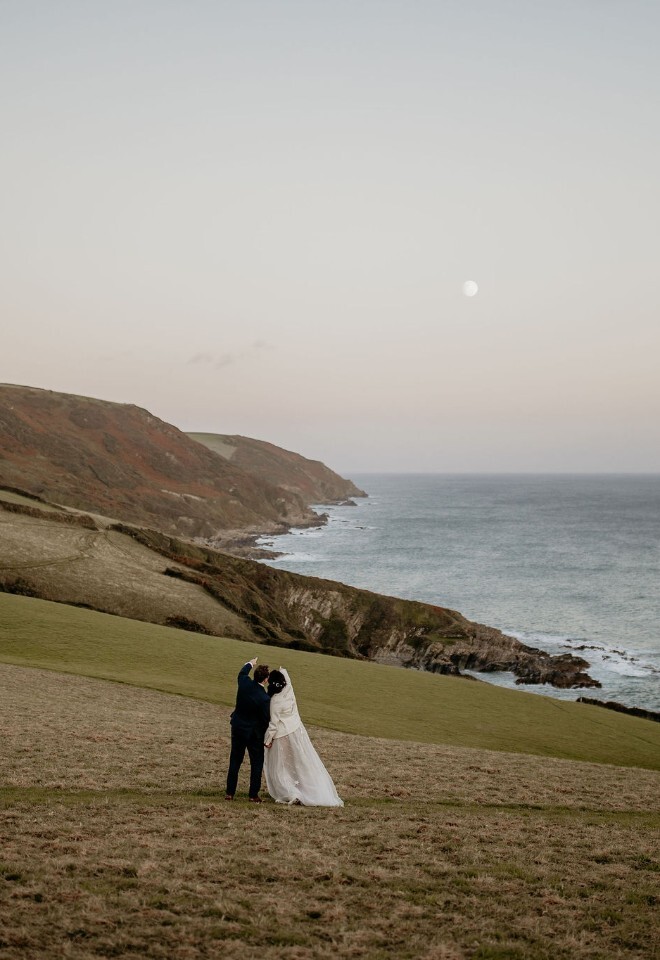 Couple looking at the view along a coastal hillside in wedding attire, holding hands