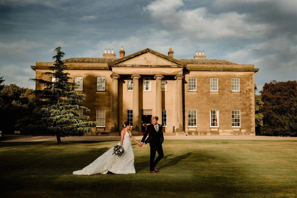 Married couple walking through the grounds in front of the exterior building of Rise Hall wedding venue, Hull.