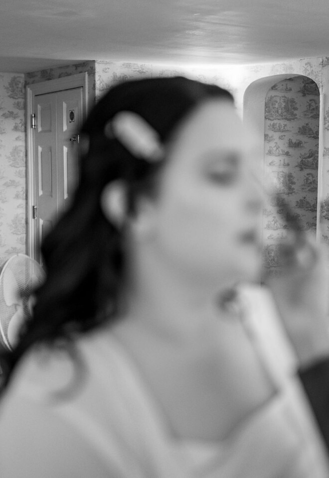 Bride getting ready with bridesmaids relaxing in the background, candid moment in black and white.