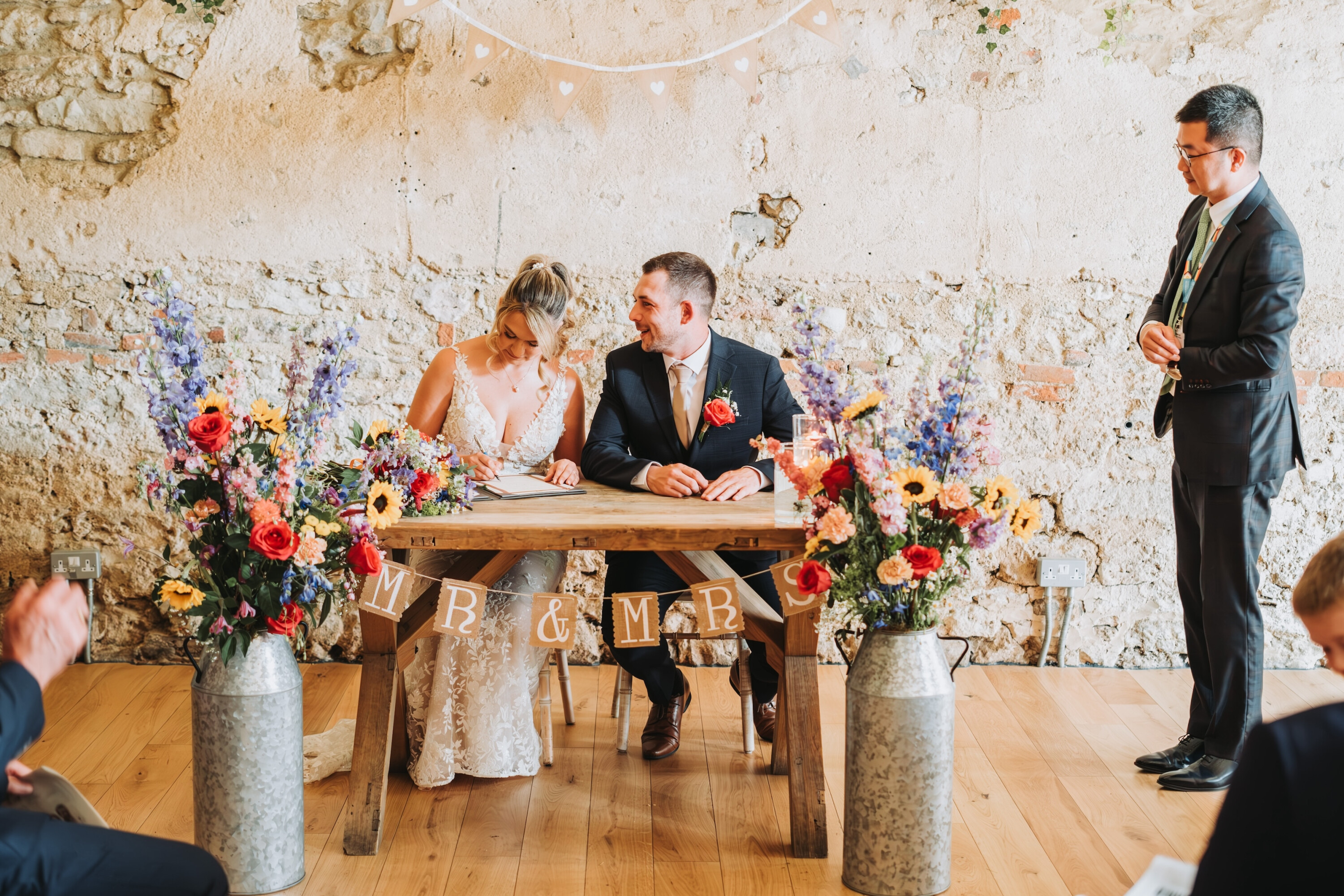 Bride and groom signing their marriage certificate at The Crown and Thistle Barn with colourful floral displays