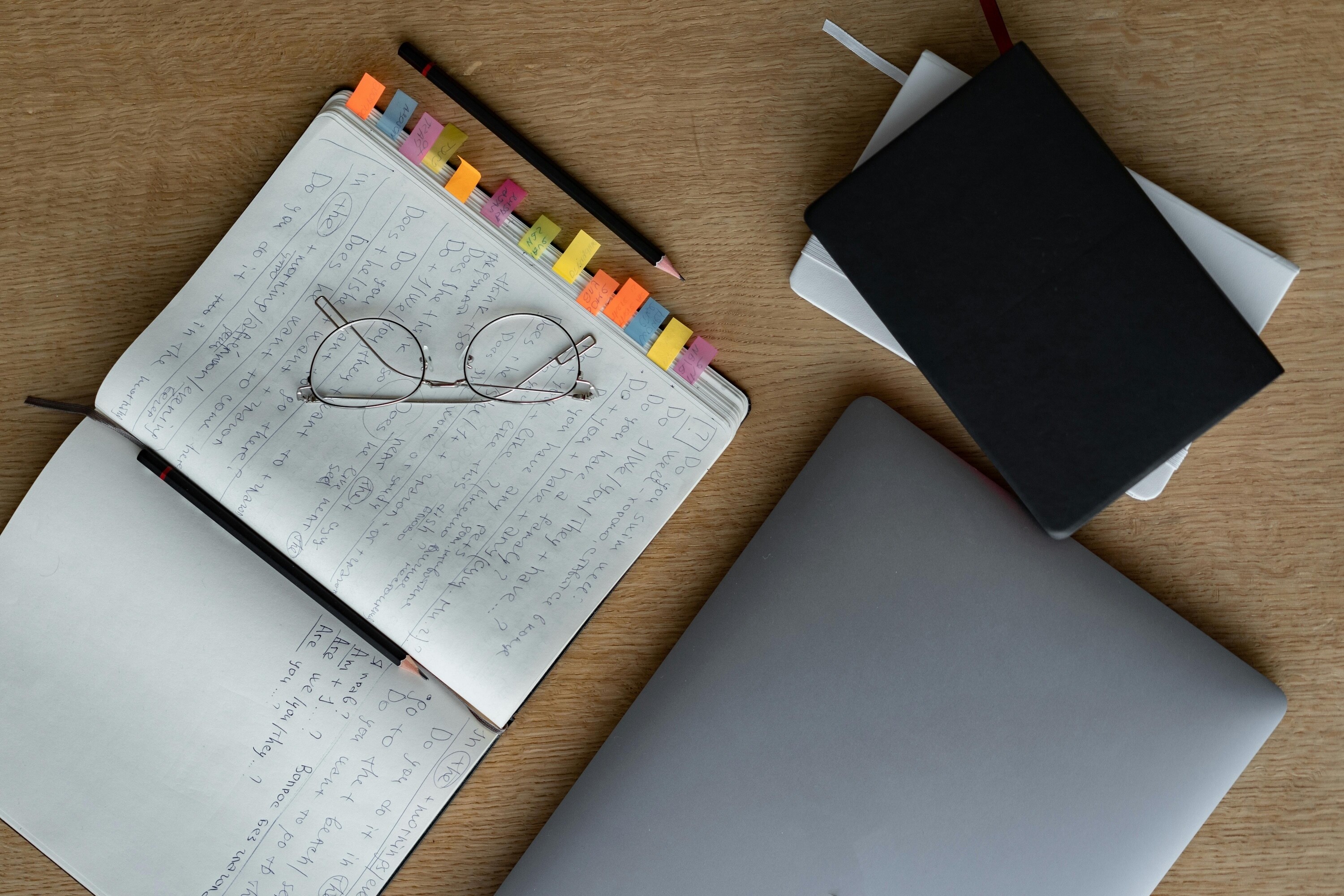 Wedding planning notebook and checklist beside a laptop and stationery on a wooden table.