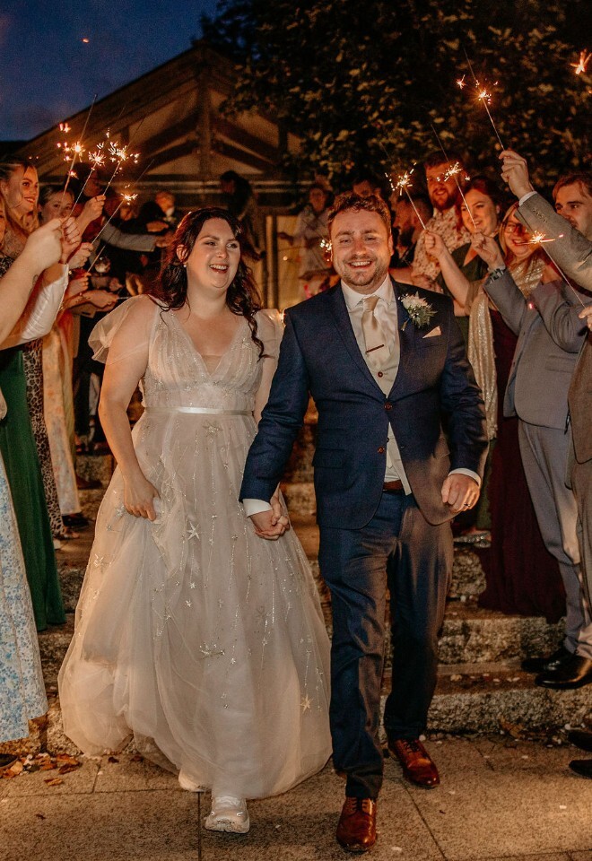 Couple walking through a sparkler send-off at night surrounded by guests.