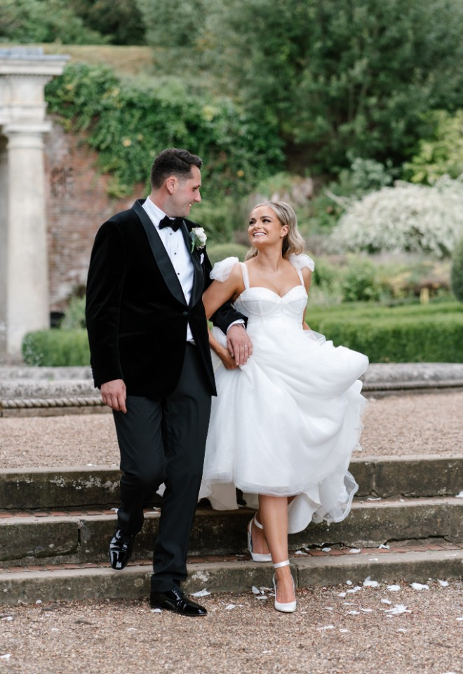 Bride and groom walking through venue grounds. They smile at eachother