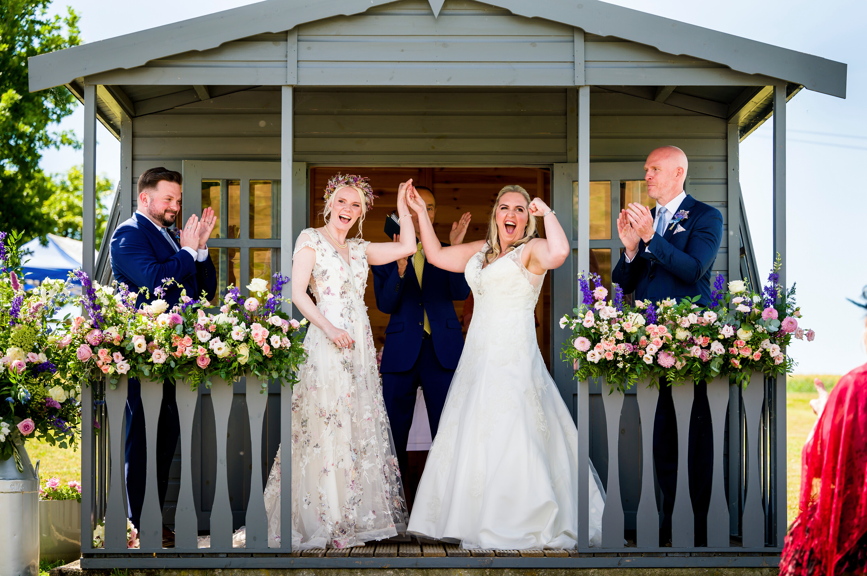 Bride and bride celebrate at the alter surrounded by summer flowers