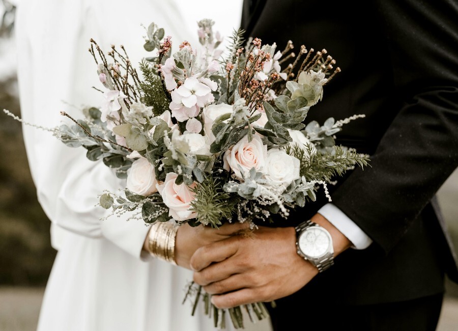 Bride and grooms hands holding a bouquet of flowers