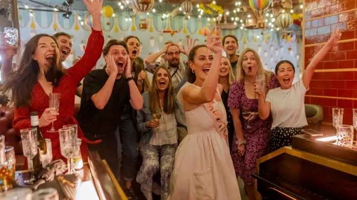Bride celebrating with friends during a hen party at Flight Club Darts, cheering and raising their arms in a colourful bar setting.